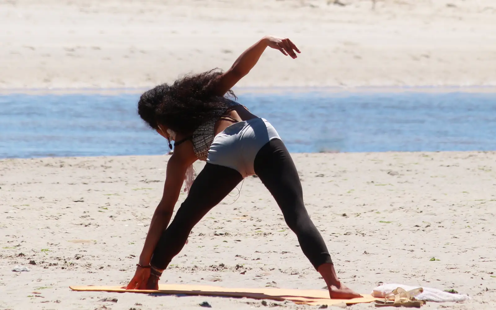 A woman in triangle pose on a sandy beach with the sea behind her